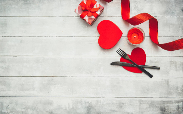 Valentine's day table setting with  fork, knife, red hearts, ribbon and roses. Valentines day background or first date - Fotó, kép