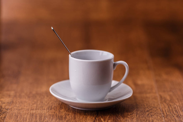 одна біла чашка кави з ложкою на білій тарілці на темно-коричневому дерев'яному фоні
 - Фото, зображення