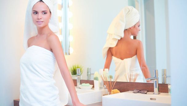 Young attractive woman standing in front of bathroom mirror - Фото, изображение