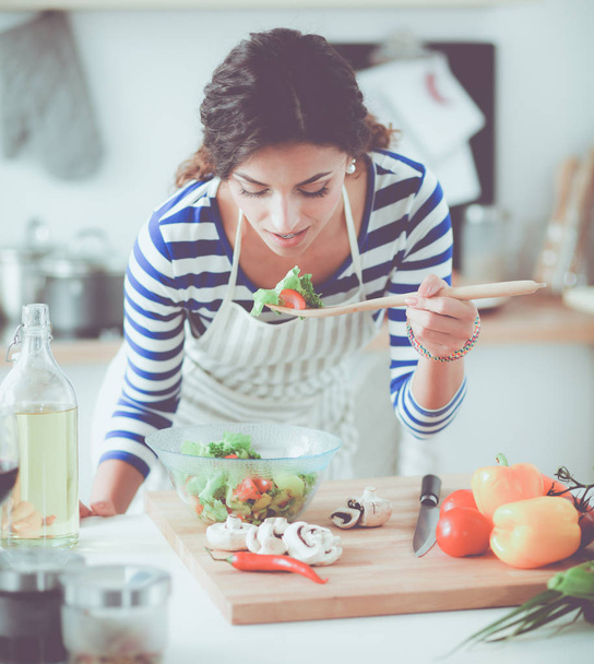 Νεαρή γυναίκα τρώει φρέσκια σαλάτα στη σύγχρονη κουζίνα - Φωτογραφία, εικόνα