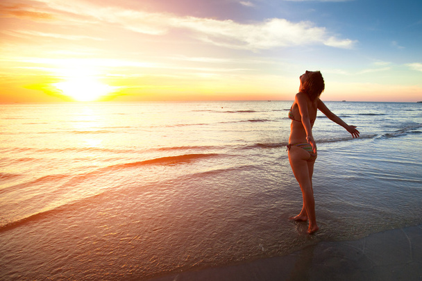 若い女性美しい夕日時のビーチの上に立つ - 写真・画像