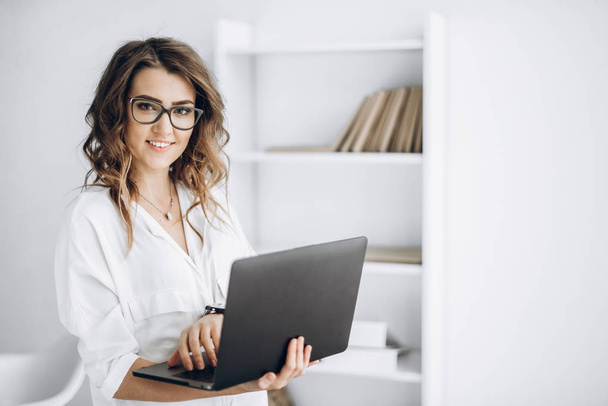 Giovane bella donna d'affari in occhiali lavora sul computer portatile nel suo ufficio
 - Foto, immagini
