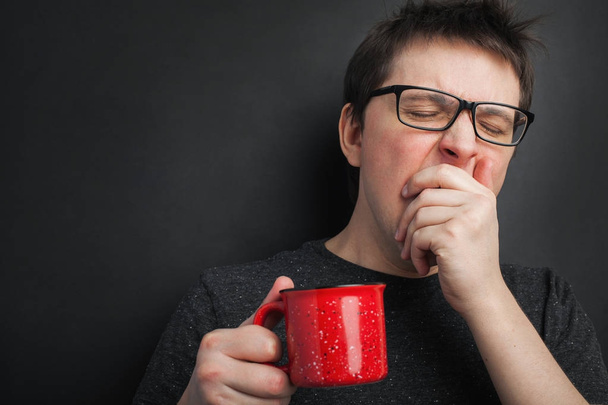 Homem bocejo sonolento em óculos com xícara vermelha de chá ou café tem cabelos não penteados em roupas íntimas no fundo preto, refresco matinal e bebida. Copiar espaço para o seu texto
 - Foto, Imagem