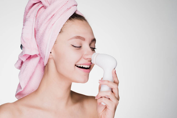 woman with a towel cleanses the skin on her face with an electric brush - Φωτογραφία, εικόνα