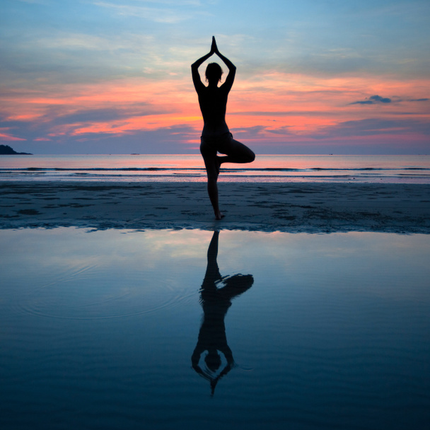 mladá žena cvičí jógu při západu slunce na pobřeží, odraz ve vodě - Fotografie, Obrázek