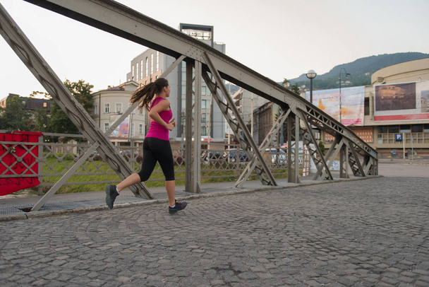 young sporty woman jogging across the bridge at sunny morning in the city - Foto, imagen