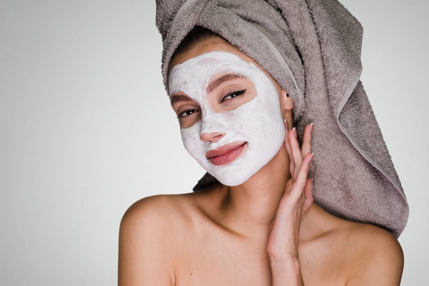 happy woman with a towel on her head apply a cleansing mask on her face - Foto, Imagen