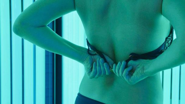 Young woman enters the tanning booth and removes a bra on the move. - Photo, image