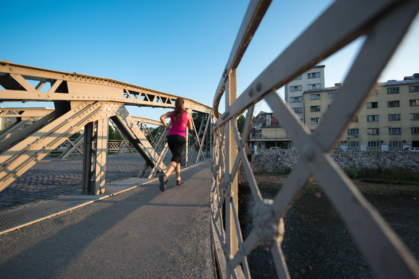 young sporty woman jogging across the bridge at sunny morning in the city - Foto, Imagen