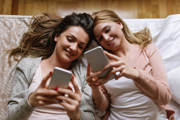 Gorgeous friends using the mobile in the bedroom. - Фото, изображение