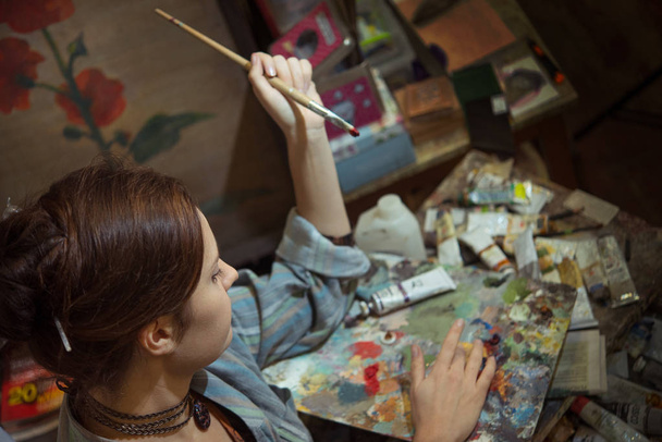 Young woman artist painting with oil paints in the studio workshop - Photo, Image