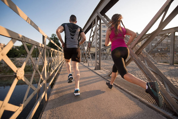 urban sports, healthy young couple jogging across the bridge in the city at sunny morning - Fotó, kép