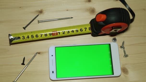 Uno smartphone con display verde, un metro a nastro da costruzione e viti
. - Filmati, video