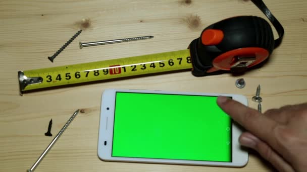 Uno smartphone con display verde, un metro a nastro da costruzione e viti
. - Filmati, video