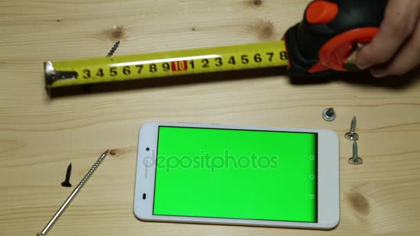 Een smartphone met een groene display, een meetlint bouw en schroeven. - Video