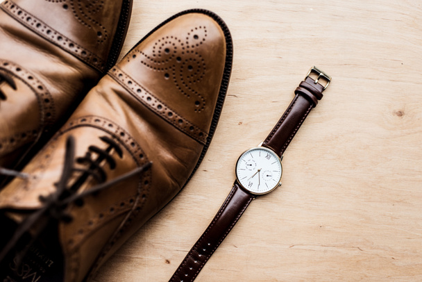 top view of brown shoes and watch on wooden surface - Foto, Bild