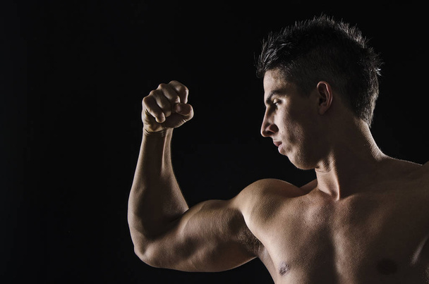 Strong guy looking in his biceps and holding fist. - Фото, изображение