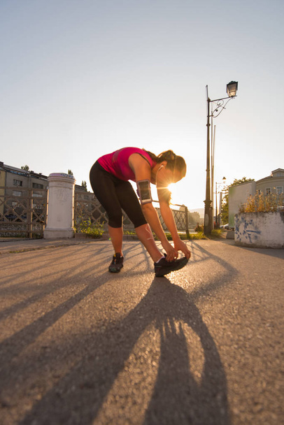 athlete woman warming up and stretching while preparing for running on the city street at  sunny morning - Photo, Image