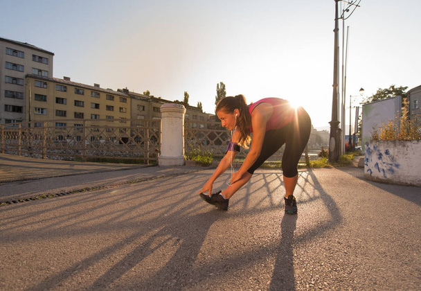 athlete woman warming up and stretching while preparing for running on the city street at  sunny morning - Foto, Bild