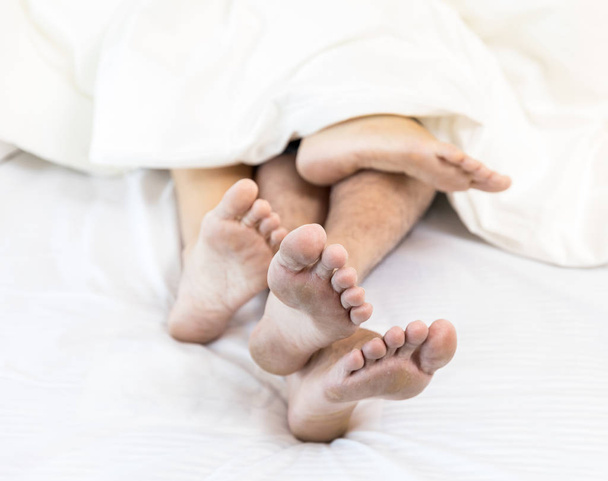 young sexy couple in love lying in bed in hotel, embracing on white sheets, close up legs, romantic mood - Φωτογραφία, εικόνα