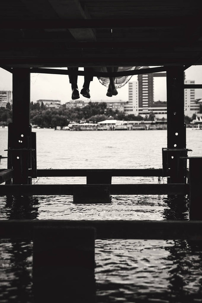 The newlyweds are sitting on the pier of the river and lowered t - Photo, Image