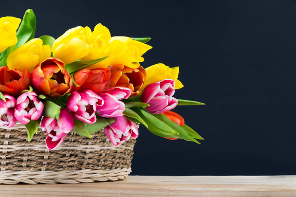 basket of tulips on a black background, on a wooden table - Фото, изображение