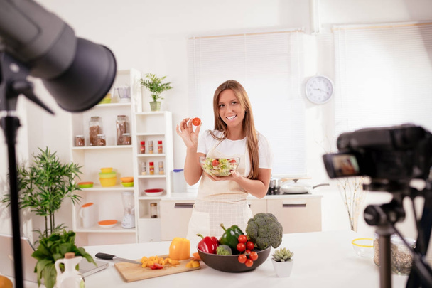 Hermosa mujer joven filmando su blog transmitido sobre comida saludable en el hogar
. - Foto, imagen
