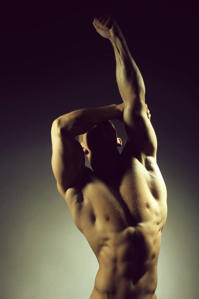 Sexy muscular male torso of athlete bodybuilder posing in power with veins on hands and bare chest on grey background - Valokuva, kuva