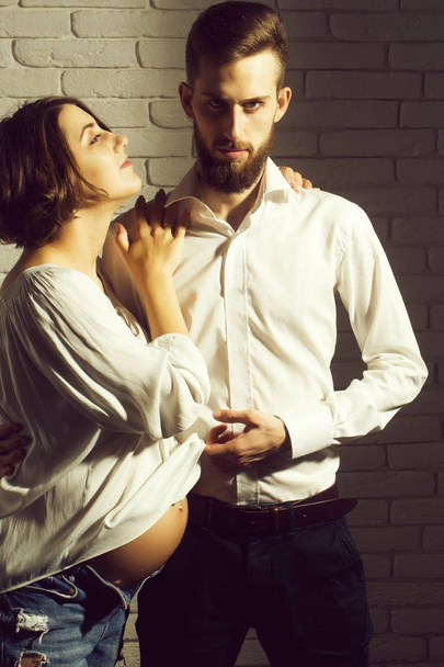 family parent couple of pretty happy sexy woman or cute pregnant girl with round belly or abdomen and handsome bearded man hipster in white shirt on brick wall background at mothers day - Foto, Bild