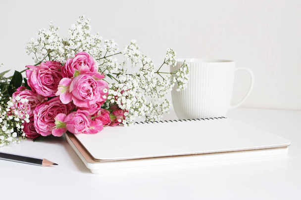 Wedding styled stock photo. Still life with pink roses, babys breath Gypsophila flowers, white cup, pencil and notebook. Floral composition. Image for blog or social media. - Фото, изображение