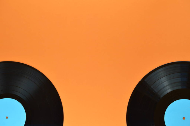 twee oude zwarte vinyl records met lege cyaan etiketten op de randen van de oranje achtergrond - Foto, afbeelding