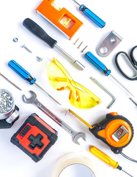 Top view of working tools, wrench, screwdriver, level, tape measure, bolts, and safety glasses on a white background. - Fotoğraf, Görsel