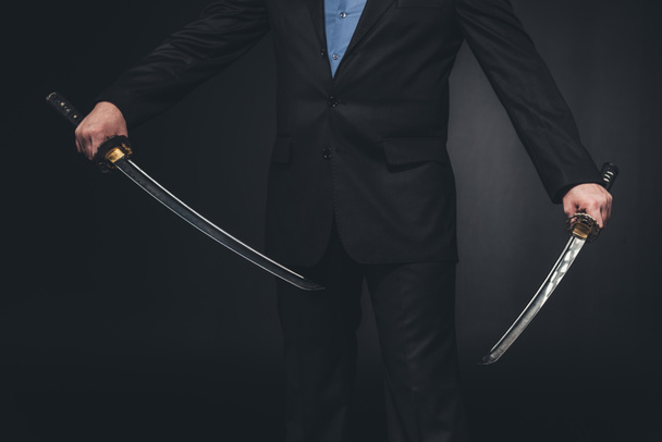 Geschossener Mann im Anzug mit doppelten Katana-Schwertern auf Schwarz - Foto, Bild