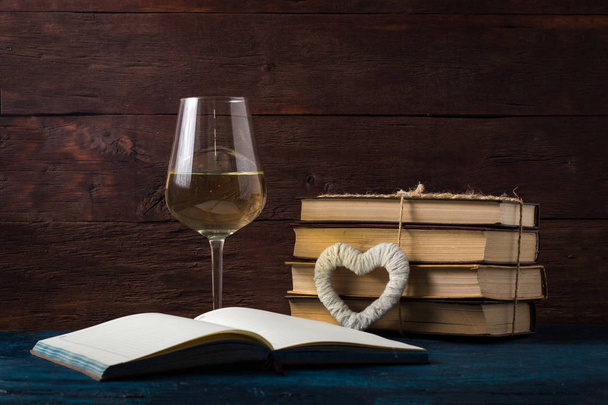 Glas mit Wein, aufgeschlagenes Buch, weißes Herz auf dem blauen Tisch - Foto, Bild