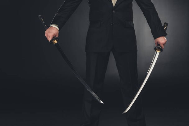 Schnappschuss eines Mannes im Anzug mit zwei Katana-Schwertern auf dunklem Hintergrund - Foto, Bild
