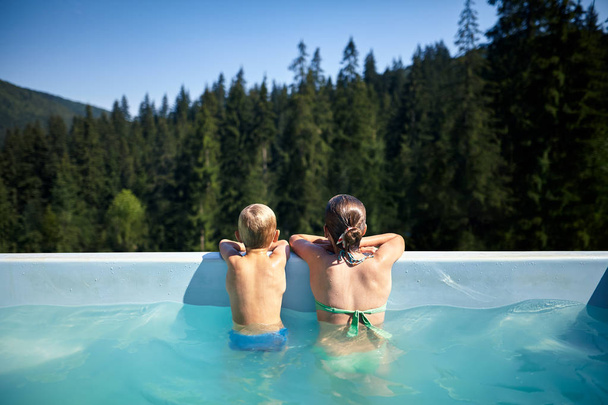 Children in pool looking at picturesque view. Brother and sister relax in pool in the open air at the weekend. Family portrait on vacation and rest, back view - Photo, Image