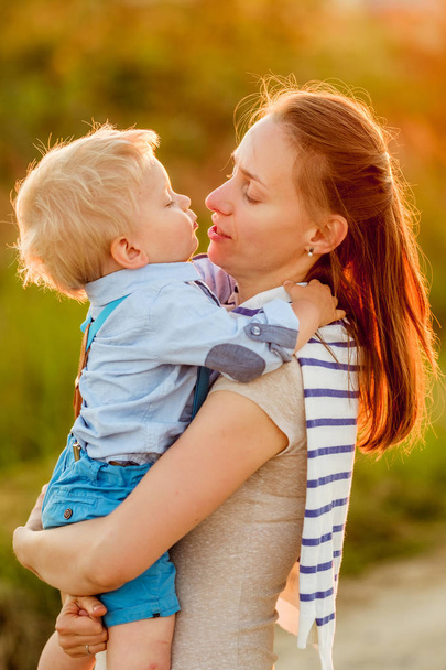 glückliche Frau und Kind, die Spaß im Freien haben. Familienleben ländliche Szene von Mutter und Sohn im Sonnenuntergang. Junge küsst seine Mutter.  - Foto, Bild