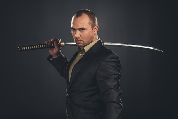 serious man in suit with katana sword isolated on black - 写真・画像