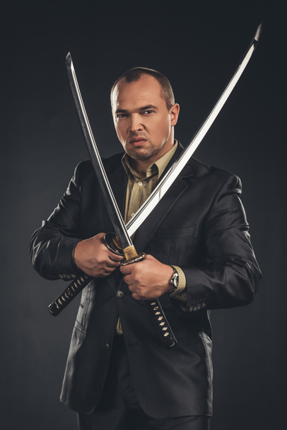 angry man in suit with katana sword isolated on black - Photo, Image