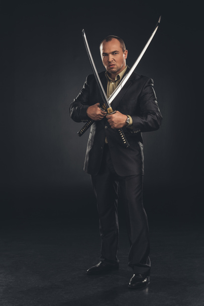 pohledný muž v obleku s duální katana meče na černém pozadí - Fotografie, Obrázek