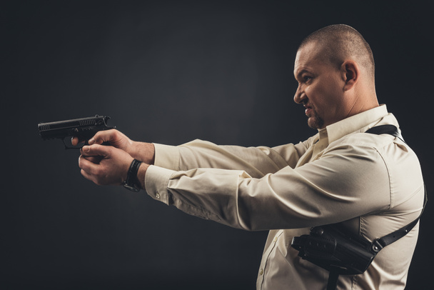 黒に分離された銃を保持しているシャツを着た男性の側面図 - 写真・画像