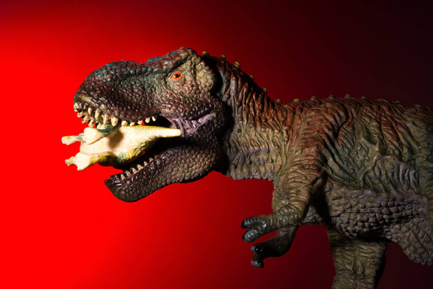 tiranosaurio mordiendo un dinosaurio más pequeño con luz de punto en la cabeza y luz roja en el fondo
 - Foto, imagen