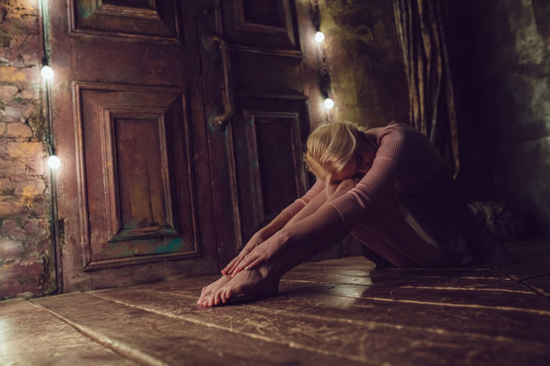 Beautiful blonde woman is sitting on the wooden floor. - 写真・画像