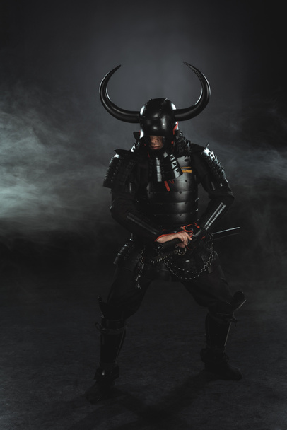armored samurai taking out his katana on dark background with smoke - Photo, Image