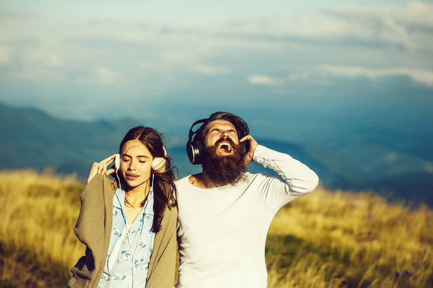 Young couple of pretty girl covered in blanket and bearded man hipster with beard listen to music with headphones on mountain scene - Foto, Imagem