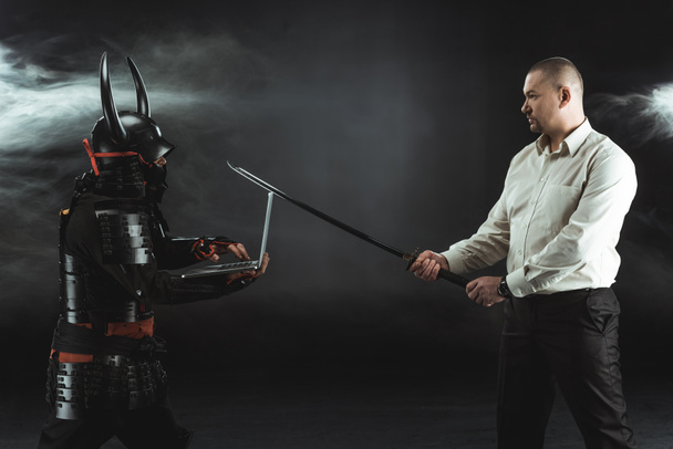 boční pohled na člověka s katana stojící v předním samuraje, zatímco on pomocí přenosného počítače - Fotografie, Obrázek