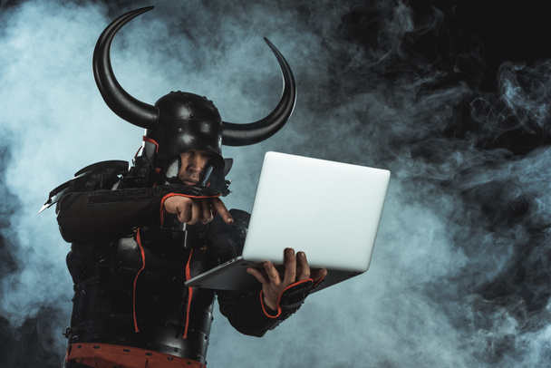 armored samurai using laptop on dark background with smoke - Photo, Image