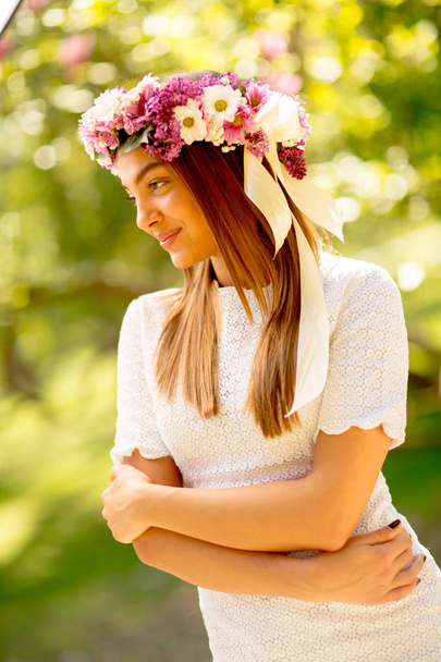 Porträt einer jungen Frau mit einem Kranz frischer Blumen auf dem Kopf - Foto, Bild