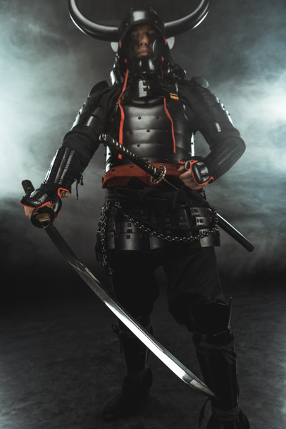 samurai in traditional armor with swords on dark background with smoke - Photo, Image