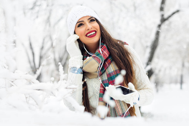 Woman listening music with her mobile phone in first snow - Foto, Imagem